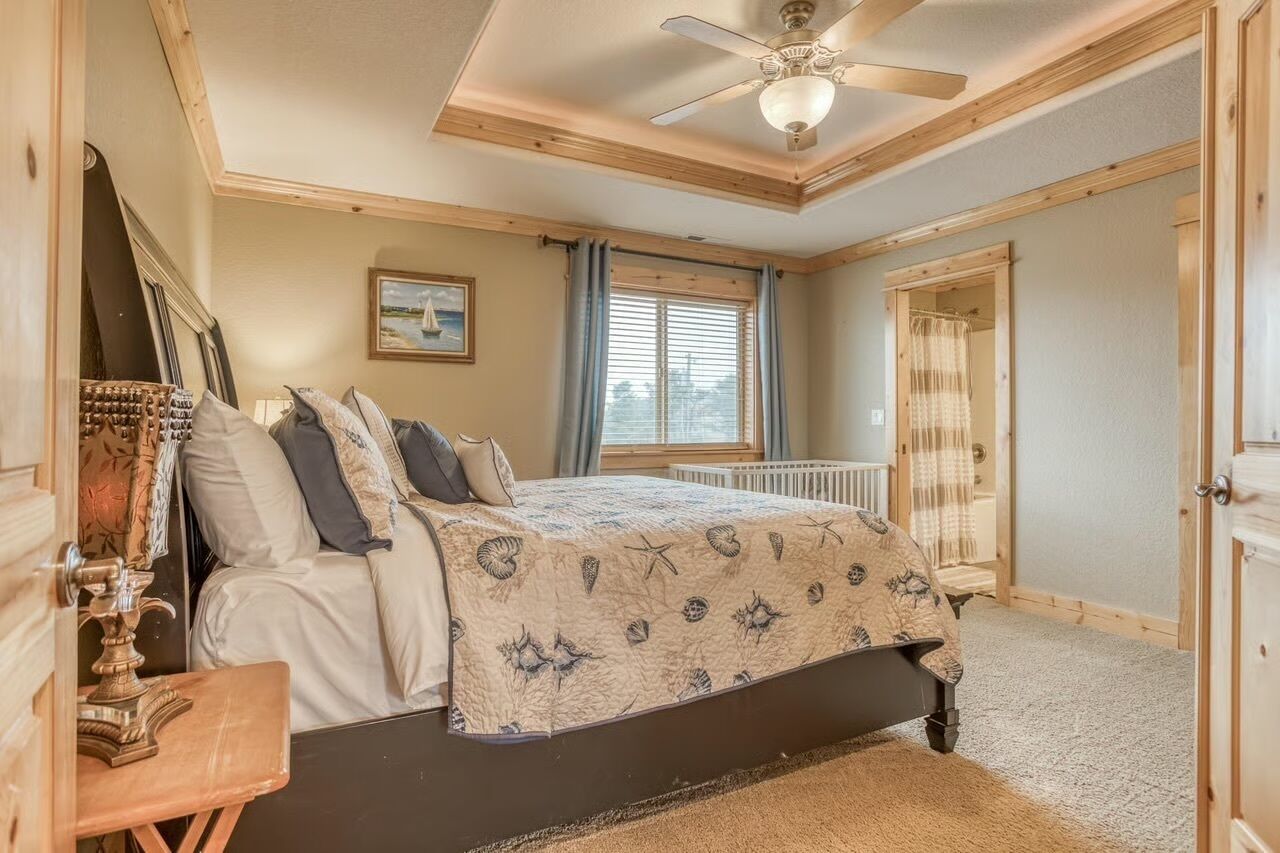 A bedroom with a bed, a ceiling fan, a window with curtains, and a door.