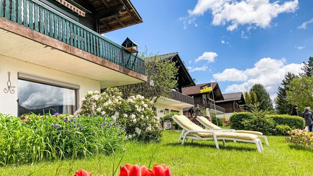 En traditionel chalet med balkon, en have med røde tulipaner og en klar, blå himmel.