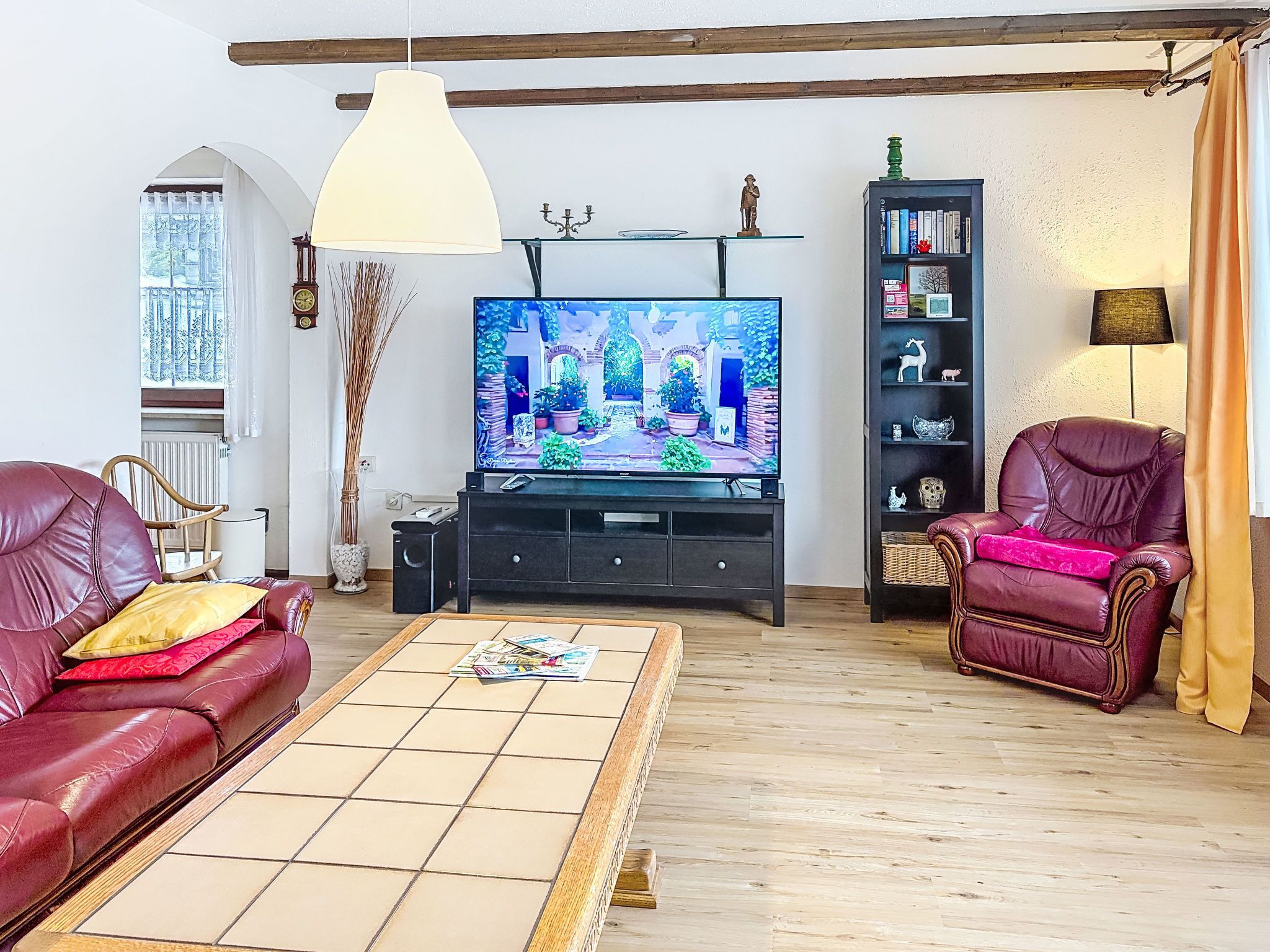 A living room with a television, leather sofas, a coffee table, a bookshelf, and a window with curtains.