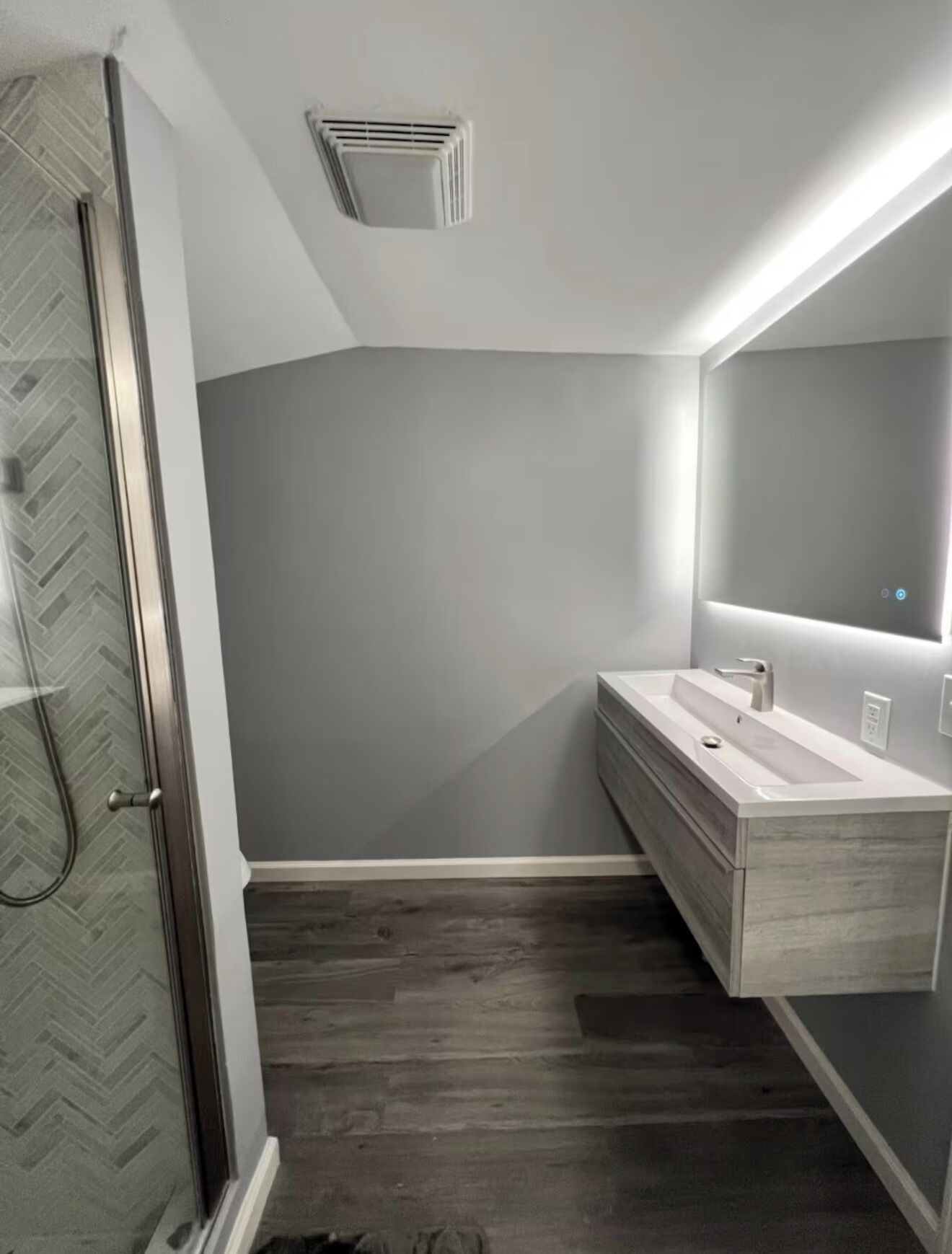 Ein modernes Badezimmer mit Dusche in Fischgrätmuster, einem großen Spiegel und einem hölzernen Waschtisch.