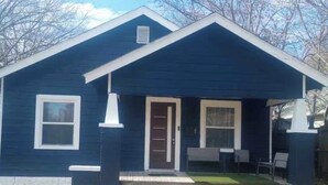Une maison de plain-pied à l’extérieur bleu foncé, avec une porte d’entrée et un petit porche doté d’un banc.