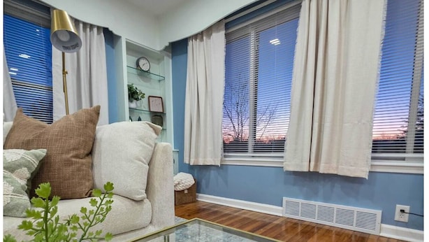 Ein Wohnzimmer mit einer Couch, einem Glastisch, einem Blumentopf und einem Fenster mit Jalousien.