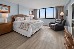 A bedroom with a bed, a chair, a dresser, and a large window with a view. - 2BR 2BA Oceanfront Bliss at Carolina Dunes (Myrtle Beach)