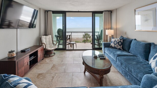 A living room with a sofa, a coffee table, a TV, and a balcony with a view of the beach. - 2BR 2BA Oceanfront Bliss at Carolina Dunes (Myrtle Beach)