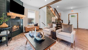 Uma sala de estar moderna com lareira, assentos confortáveis, uma escada e vista para o exterior.