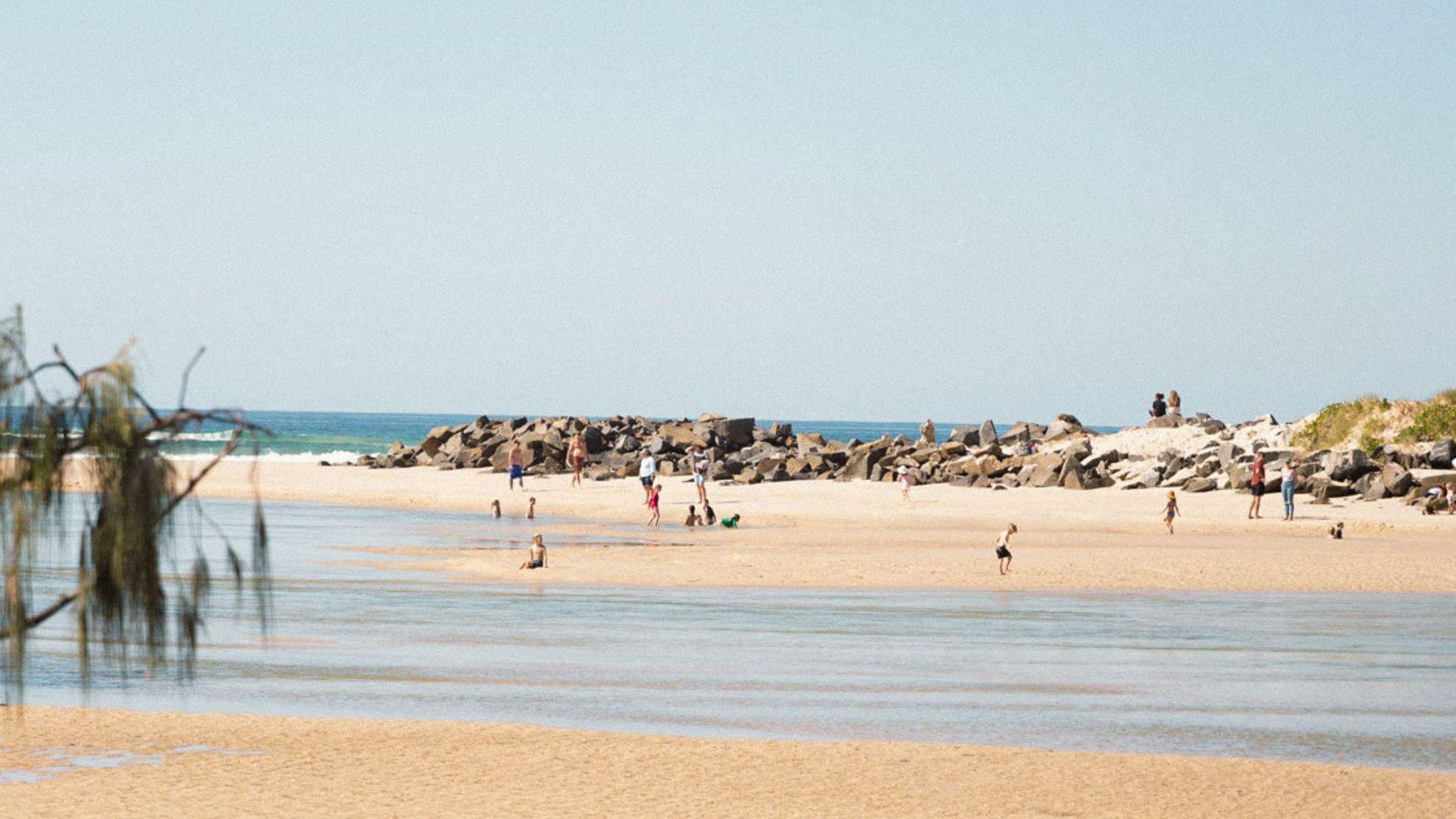 A beach with rocky outcrops and people walking along the shore.