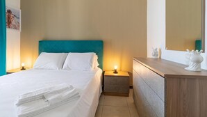 Ein ordentlich bezogenes Bett mit weißen Leinen, einem türkisblauen Kopfteil und zwei Nachttischlampen.