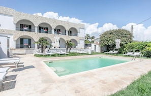 Un espace aménagé au bord de la piscine, avec des chaises longues, une piscine et un bâtiment doté de balcons en arc de cercle.