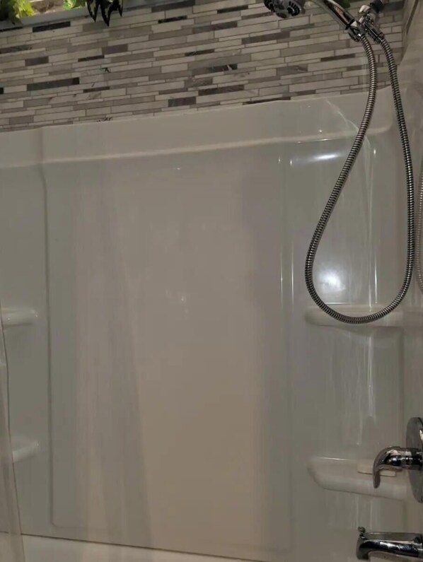 Une salle de bain moderne avec une baignoire blanche, une pomme de douche et un mur recouvert de carreaux.