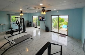 Un gimnasio con equipo de ejercicio, televisión y ventanas amplias que dan a zonas verdes.
