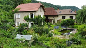 Ein zweistöckiges Haus mit rotem Dach, umgeben von üppiger Vegetation und einem kleinen Teich.