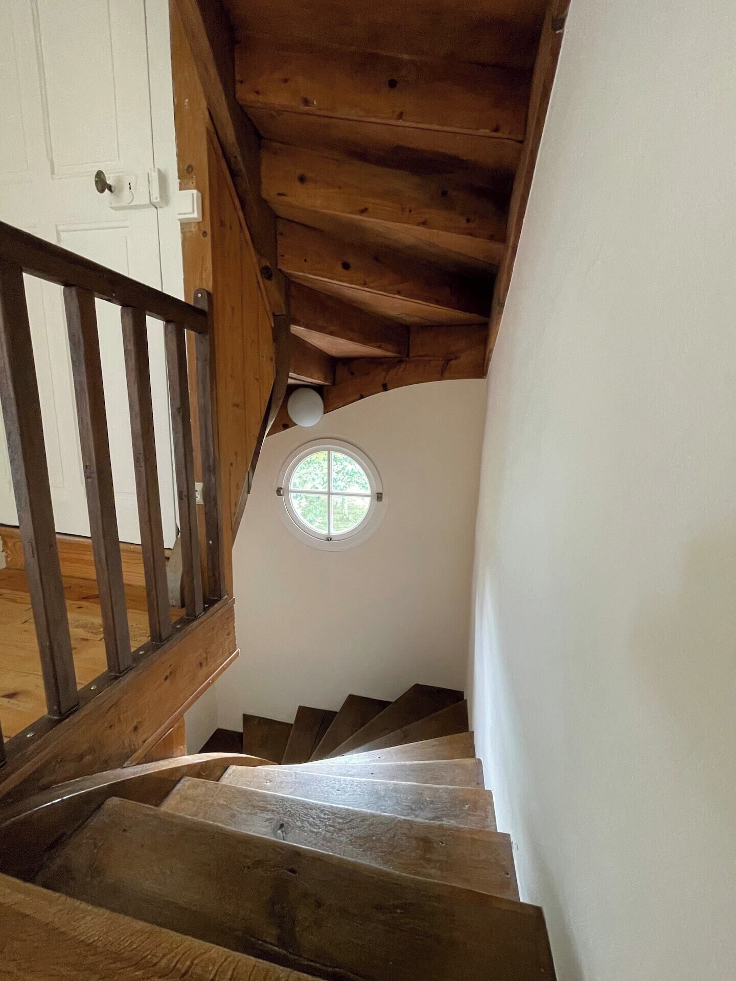 Eine Holztreppe mit einem kleinen, runden Fenster am oberen Ende.