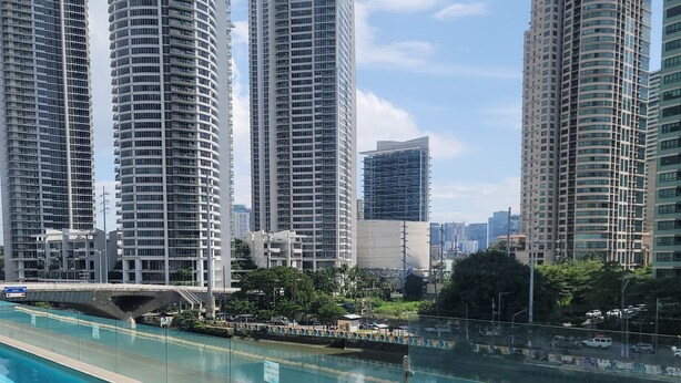 A swimming pool with clear blue water, surrounded by tall residential buildings and a bridge in the background. - Corner Unit @ Acqua  Private Residences - Livingstone Tower (Mandaluyong)