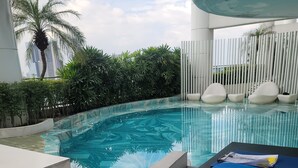A swimming pool with a curved edge, surrounded by greenery and white vertical panels. - Corner Unit @ Acqua  Private Residences - Livingstone Tower (Mandaluyong)
