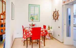 A dining area with a table set for four, a window with a view of greenery, and a ship's wheel decoration on the wall.