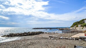 Una playa rocosa con un muelle que se adentra en el mar, cielo despejado y edificios en una colina.