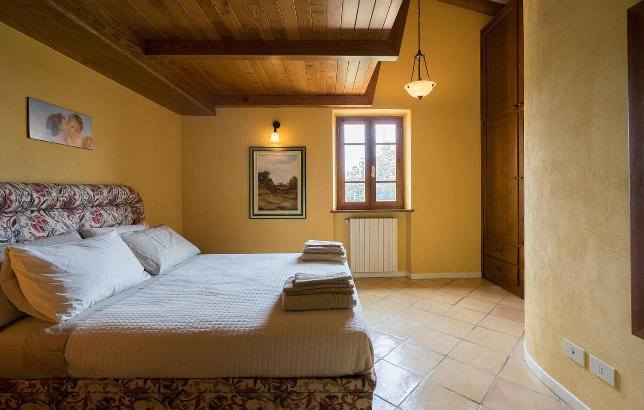 Un dormitorio con cama, ventana, radiador y un cuadro en la pared.