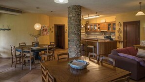 A dining area with a wooden table and chairs, a stone pillar, and a kitchen with wooden cabinets and a bar. - Cozy home in Lucignano (Lucignano)