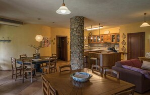 A dining area with a wooden table and chairs, a stone pillar, and a kitchen with wooden cabinets and a bar. - Cozy home in Lucignano (Lucignano)