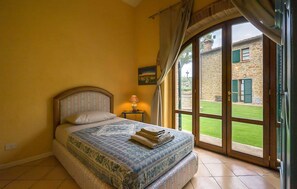 A bedroom with a bed, a nightstand, a lamp, and a view of a stone building through a glass door. - Cozy home in Lucignano (Lucignano)
