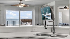 A modern kitchen with a large window overlooking the ocean, a dining area with a view, and a ceiling fan. - NEW listing! Direct Oceanfront 2/2 | Fully Updated | Heated Pool & Garage Parking (Ormond Beach)