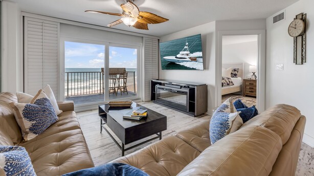 A living room with a large window, a ceiling fan, a television, and a sofa. - NEW listing! Direct Oceanfront 2/2 | Fully Updated | Heated Pool & Garage Parking (Ormond Beach)