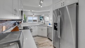 A modern kitchen with white cabinetry, stainless steel appliances, and a view to the outside. - NEW listing! Direct Oceanfront 2/2 | Fully Updated | Heated Pool & Garage Parking (Ormond Beach)