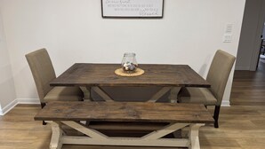 Ein Holztisch mit zwei Stühlen, eine Glasvase mit Blumen und ein gerahmtes Schild an der Wand.
