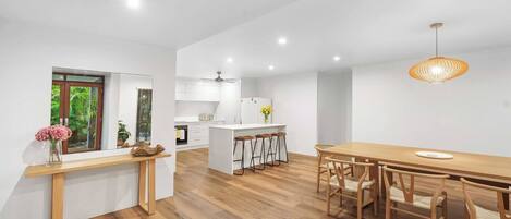A modern kitchen with white cabinets, a wooden dining table, and a hanging light fixture.