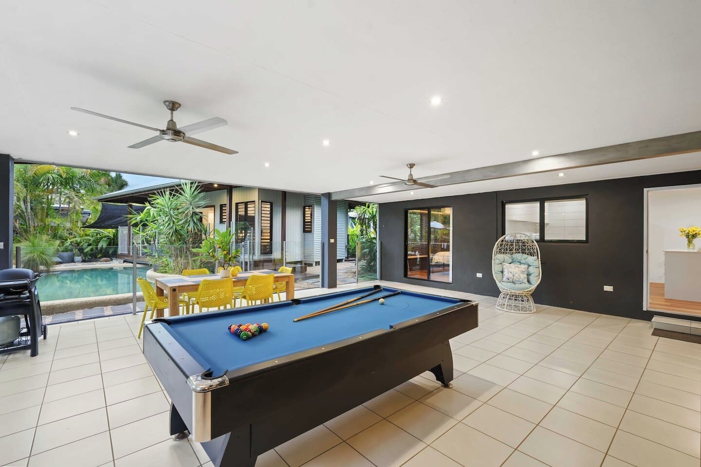 Un área de piscina interior moderna con mesa de billar, sillas amarillas y ventilador de techo.