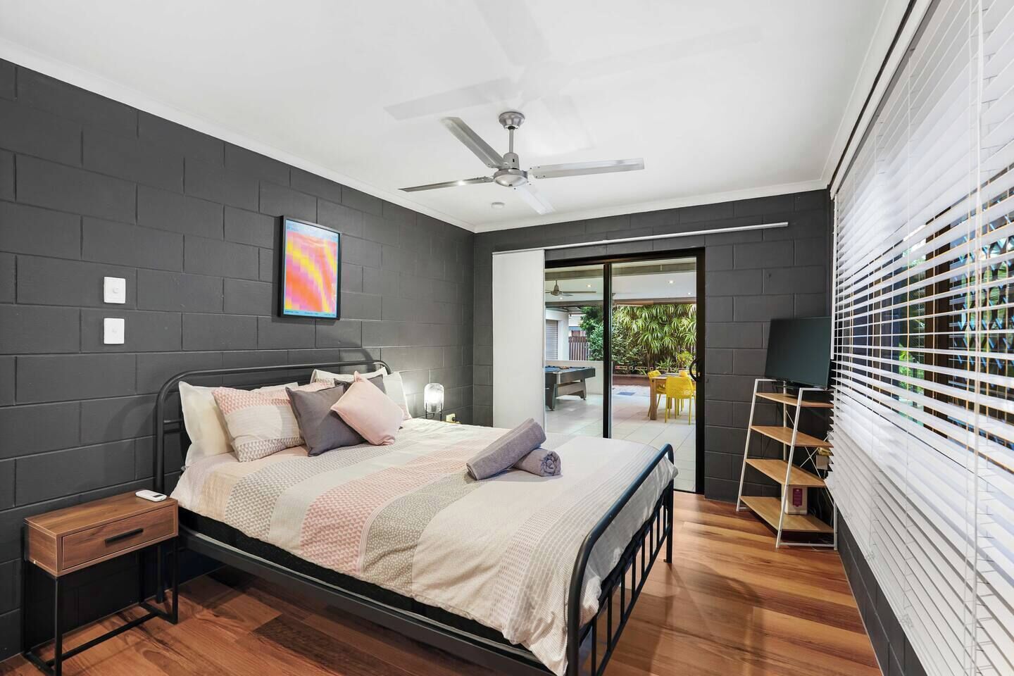Un dormitorio moderno con cama, mesitas de noche, ventilador de techo y vistas al exterior.