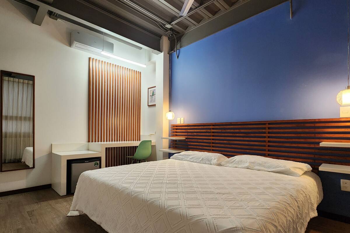 A modern hotel room with a large bed, a desk, a chair, and a wall-mounted TV.