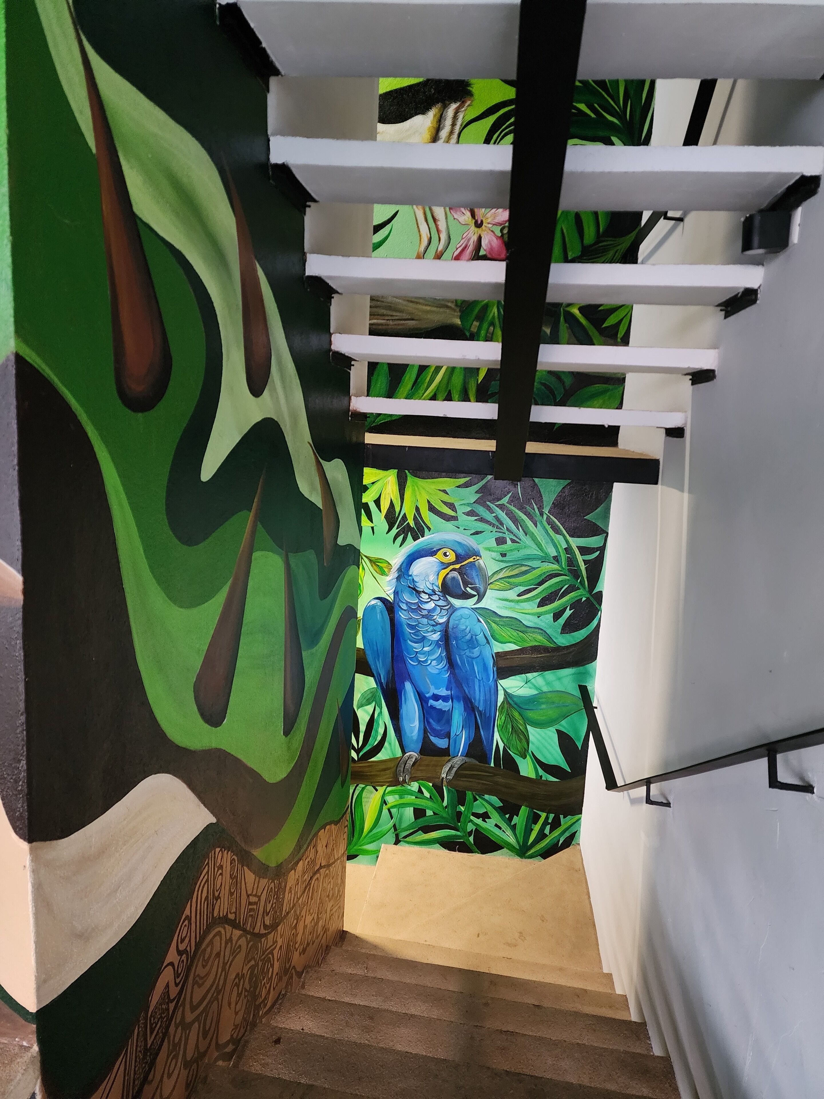 A staircase with a mural of a blue parrot on a branch, surrounded by green foliage.