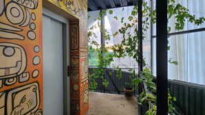 Ein überdachter Balkon mit Betonboden, eine Tür mit farbenfrohem Wandgemälde und Kübelpflanzen.