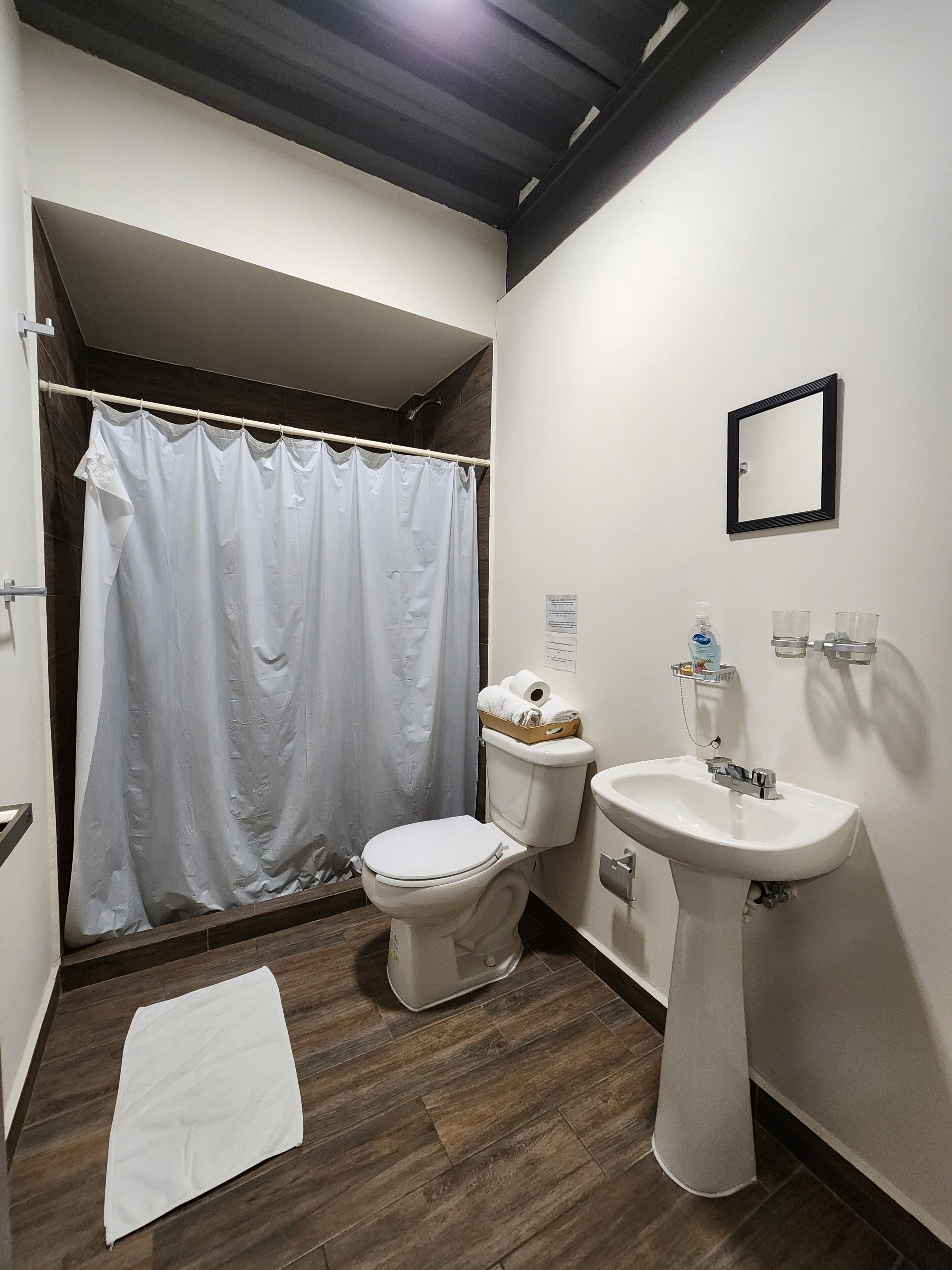 Un baño con cortina de ducha, inodoro, lavabo y una toalla en el suelo.