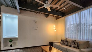 Ein modernes Wohnzimmer mit Holzboden, einer Couch mit gemusterten Kissen, einem Deckenventilator und einem kleinen Tisch.