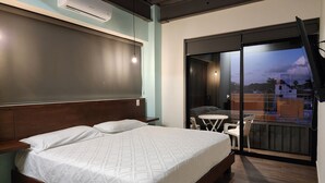Ein Schlafzimmer mit Bett, einem kleinen Tisch und einer Glasschiebetür, die auf einen Balkon führt.
