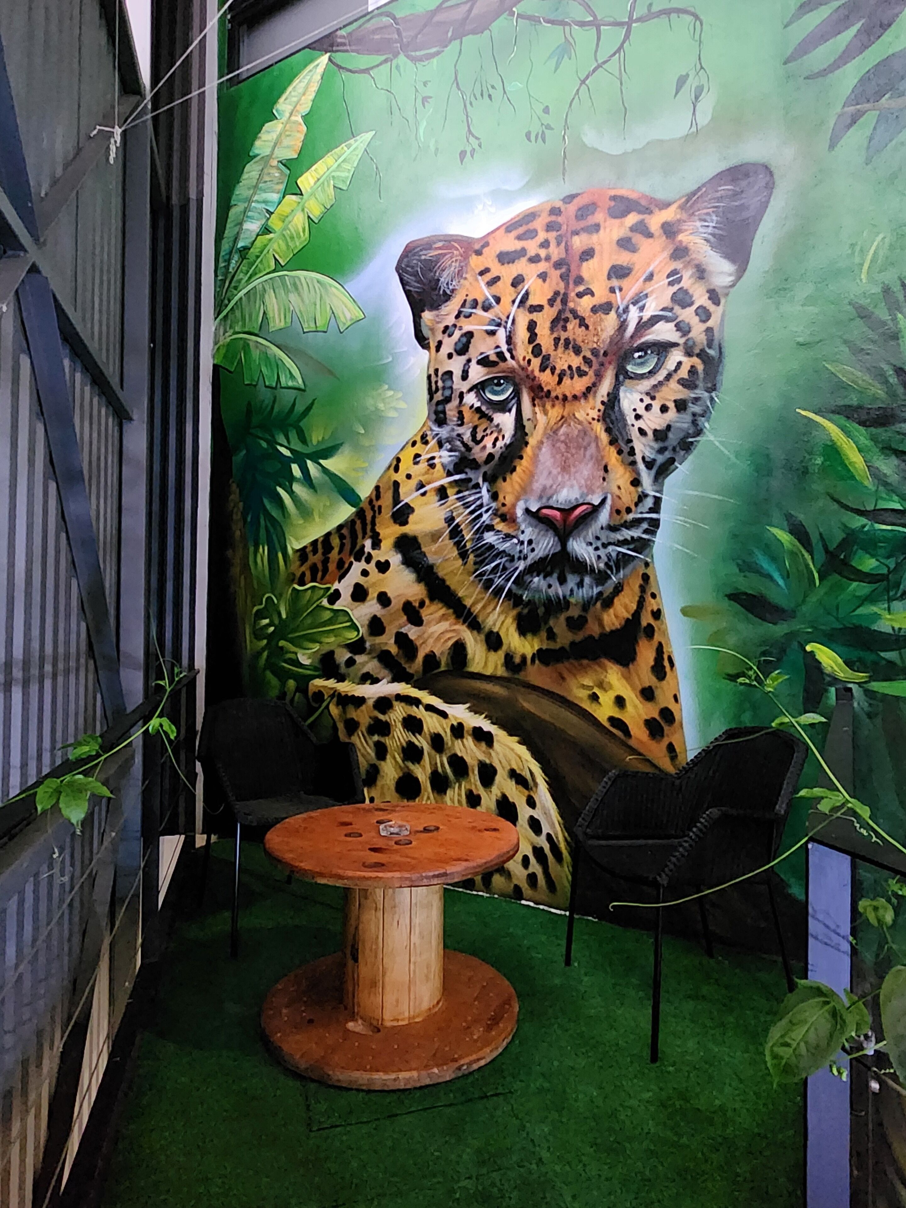 Une pièce décorée d’une fresque représentant un léopard, avec une table ronde en bois et deux chaises noires.