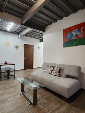 A modern living room with a grey sofa, a glass coffee table, and a wooden dining table with chairs. There are wall-mounted fans and a painting of an elephant. - Torre Yaxche Urban Center (Cancun)