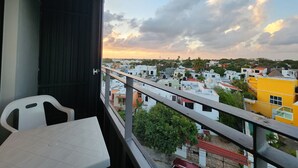 Ein Balkon mit Tisch und Stühlen, der einen Wohnbereich mit verschiedenen Gebäuden und einem Sonnenuntergangshimmel blickt.