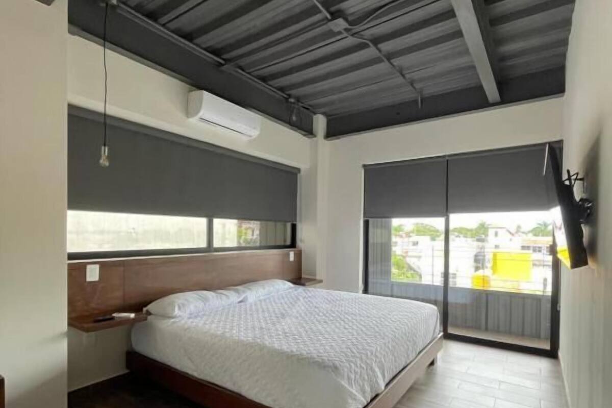A bedroom with a bed, a nightstand, a ceiling fan, and a large window with a view of the outside.