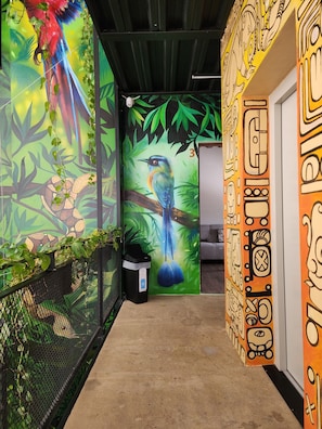 A hallway with vibrant murals, a trash bin, and a mesh fence. - Torre Yaxche Urban Center (Cancun)