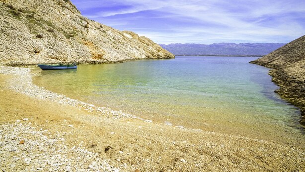 Un lago tranquilo con orilla rocosa y un bote a la izquierda.