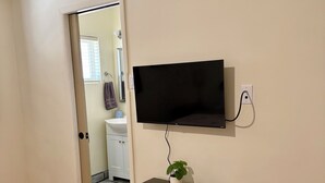 Una habitación con un televisor de pantalla plana montado en la pared, un pequeño mueble negro debajo y una planta en la parte superior.