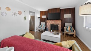 A living room with a fireplace, two armchairs, a coffee table, and a TV mounted above the fireplace. - Central STL - Near Zoo, WashU, Quiet w/ Easy Parking! (St. Louis)