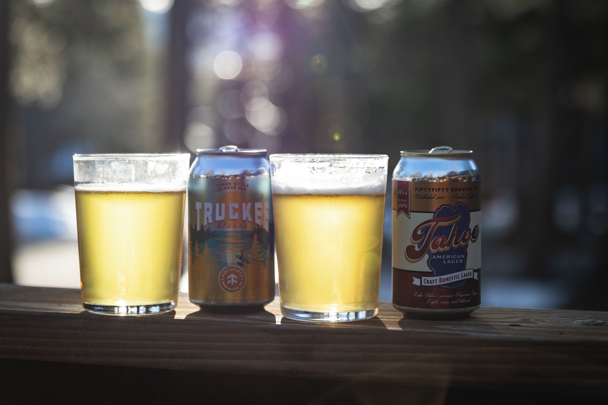 Trois verres de bière et une canette de bière sur une surface en bois.