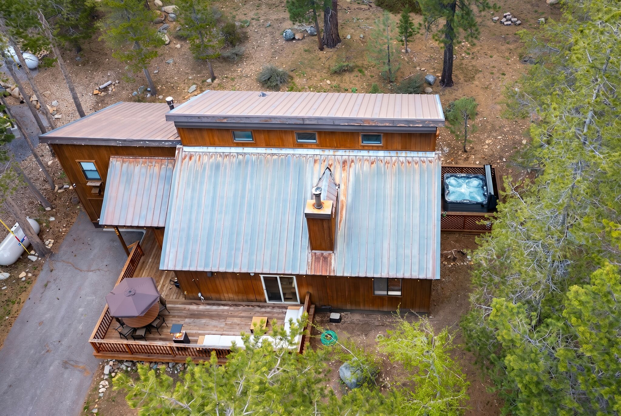 A two-story cabin with a deck, a hot tub, and a clear view of the surrounding forest.