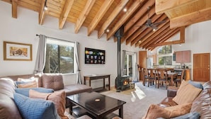 Een ruime woonkamer met een hoog houten plafond, een open haard en een eethoek met houten meubels.