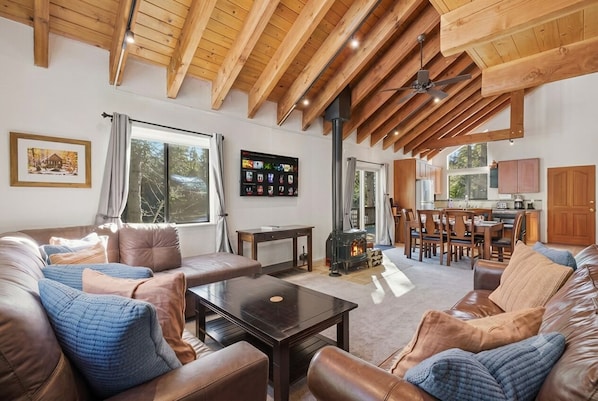 A spacious living area with a high wooden ceiling, a fireplace, and a dining area with wooden furniture. - Palisades! Spacious Living, Views & Family Fun (Tahoe City)
