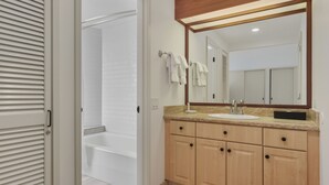 Un baño con bañera, lavamanos, armarios de madera y un espejo.